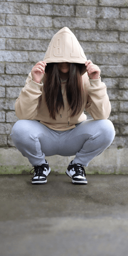 Model crouching down wearing Due Hood Tan